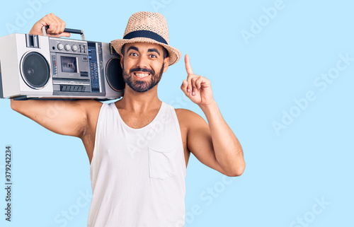 Young hispanic man holding boombox, listening to music surprised with an idea or question pointing finger with happy face, number one