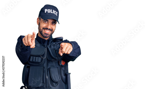 Young hispanic man wearing police uniform pointing to you and the camera with fingers, smiling positive and cheerful