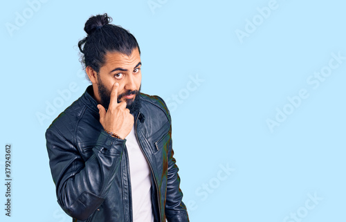 Young arab man wearing casual leather jacket pointing to the eye watching you gesture, suspicious expression