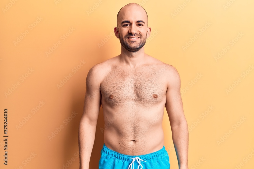 Young handsome bald man wearing swimwear shirtless with a happy and cool smile on face. lucky person.