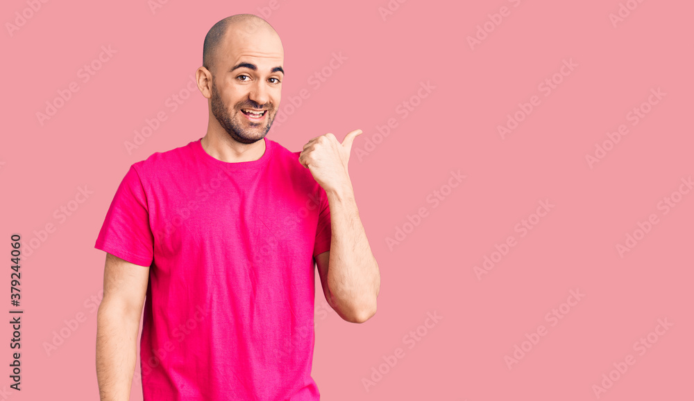 Young handsome man wearing casual t shirt smiling with happy face looking and pointing to the side with thumb up. Young handsome man wearing casual t shirt smiling with happy face looking and pointing to the side with thumb up.