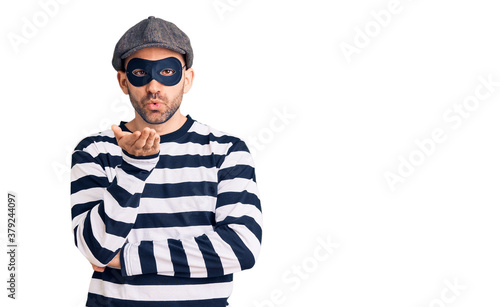 Young handsome man wearing burglar mask looking at the camera blowing a kiss with hand on air being lovely and sexy. love expression.