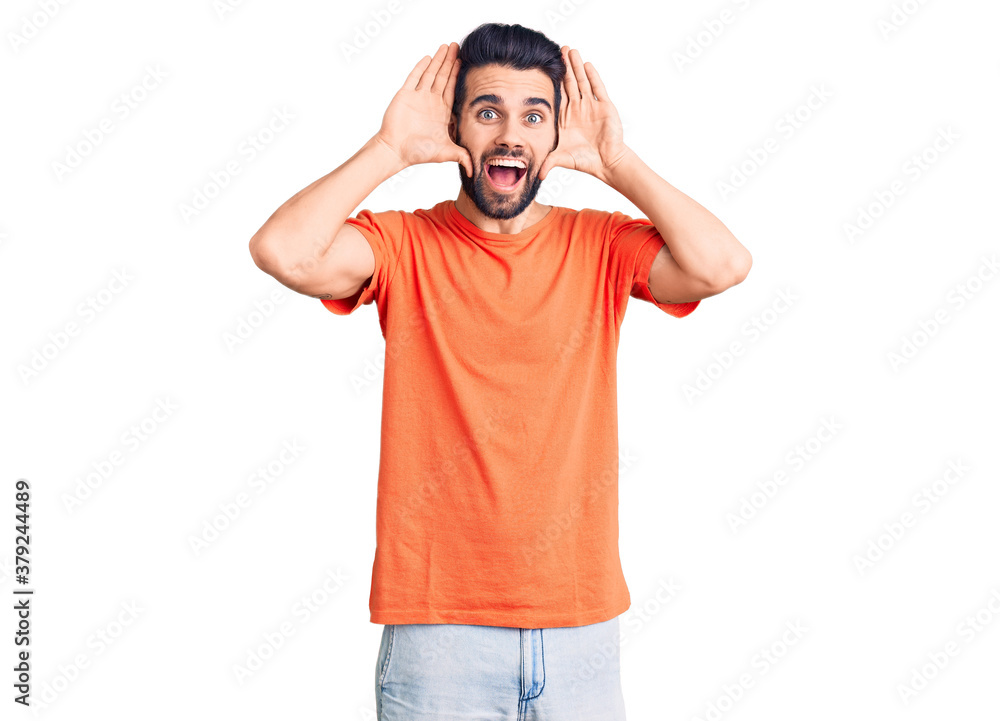 Young handsome man with beard wearing casual t-shirt smiling cheerful playing peek a boo with hands showing face. surprised and exited Young handsome man with beard wearing casual t-shirt smiling cheerful playing peek a boo with hands showing face. surprised and exited