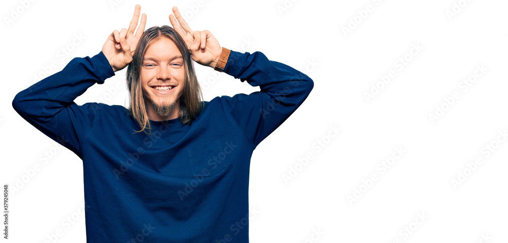 Handsome caucasian man with long hair wearing casual winter sweater posing funny and crazy with fingers on head as bunny ears, smiling cheerful Handsome caucasian man with long hair wearing casual winter sweater posing funny and crazy with fingers on head as bunny ears, smiling cheerful