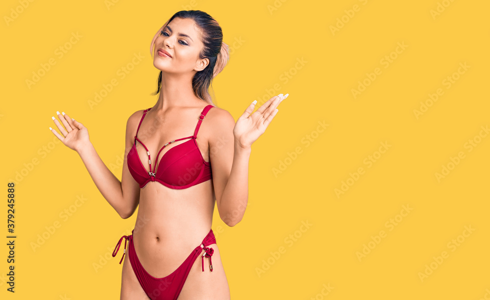 Young beautiful woman wearing bikini clueless and confused expression with arms and hands raised. doubt concept. Young beautiful woman wearing bikini clueless and confused expression with arms and hands raised. doubt concept.
