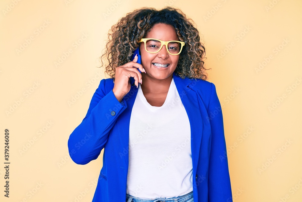 Young african american plus size woman wearing glasses having conversation talking on the smartphone looking positive and happy standing and smiling with a confident smile showing teeth Young african american plus size woman wearing glasses having conversation talking on the smartphone looking positive and happy standing and smiling with a confident smile showing teeth