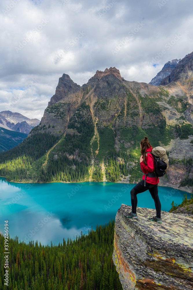 Hiker woman on top of Opabin Prospect overlooking Lake O'Hara and Mary Lake with the Canadian Rockies in the background. British Columbia, Canada