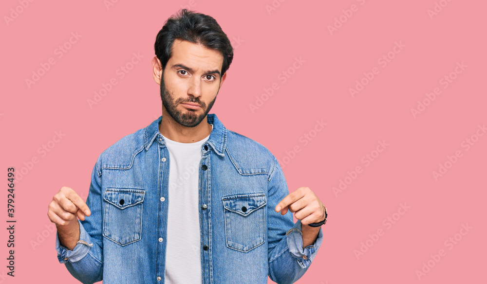 Fototapeta premium Young hispanic man wearing casual clothes pointing down looking sad and upset, indicating direction with fingers, unhappy and depressed.