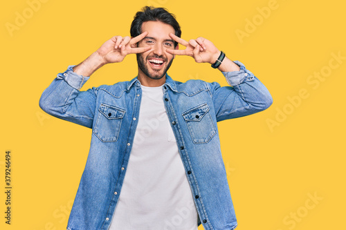 Young hispanic man wearing casual clothes doing peace symbol with fingers over face, smiling cheerful showing victory © Krakenimages.com