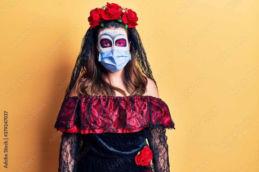 Young woman wearing day of the dead costume wearing medical mask with serious expression on face. simple and natural looking at the camera.