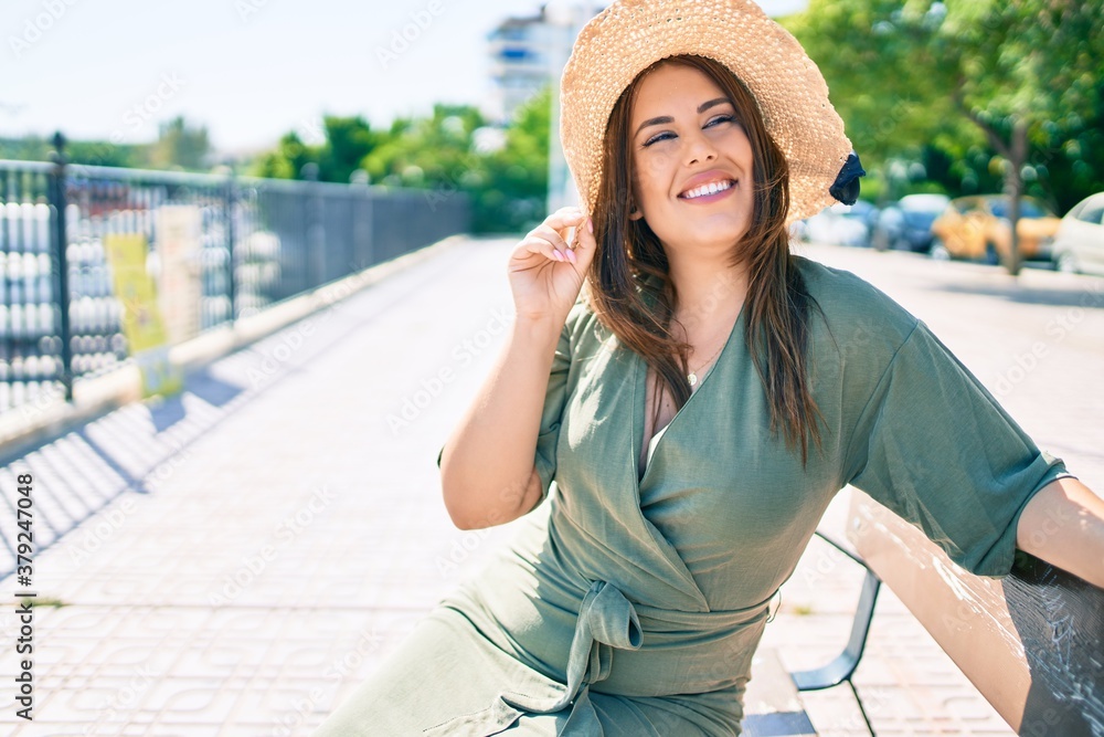 Young hispanic woman on vacation smiling happy sitting on bench at street of city