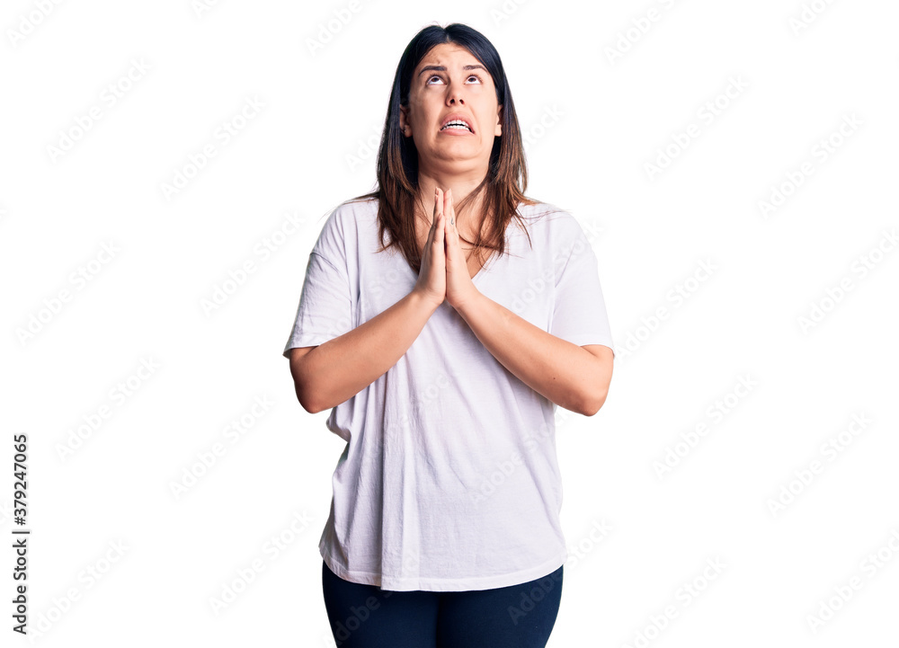 Young beautiful brunette woman wearing casual t-shirt begging and praying with hands together with hope expression on face very emotional and worried. begging. Young beautiful brunette woman wearing casual t-shirt begging and praying with hands together with hope expression on face very emotional and worried. begging.