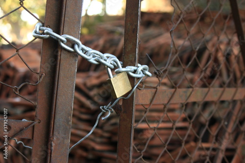 portón de hierro y alambre en exterior cerrado y oxidado con cadena de eslabones amarrados con candado  photo