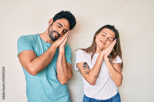 Beautiful young couple of boyfriend and girlfriend together sleeping tired dreaming and posing with hands together while smiling with closed eyes.