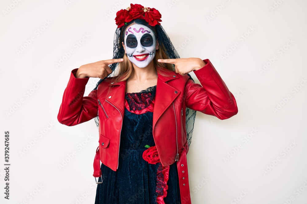 Woman wearing day of the dead costume over white smiling cheerful showing and pointing with fingers teeth and mouth. dental health concept. Woman wearing day of the dead costume over white smiling cheerful showing and pointing with fingers teeth and mouth. dental health concept.