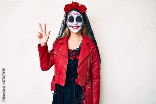 Woman wearing day of the dead costume over white showing and pointing up with fingers number three while smiling confident and happy.