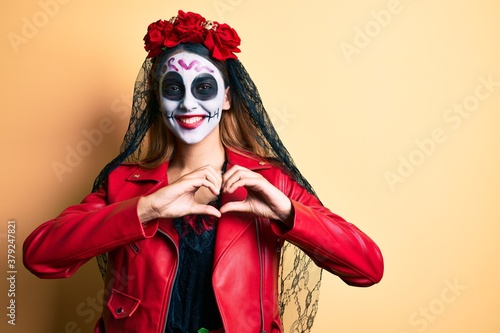 Woman wearing day of the dead costume over yellow smiling in love showing heart symbol and shape with hands. romantic concept.