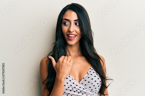 Beautiful hispanic woman wearing casual clothes smiling with happy face looking and pointing to the side with thumb up.