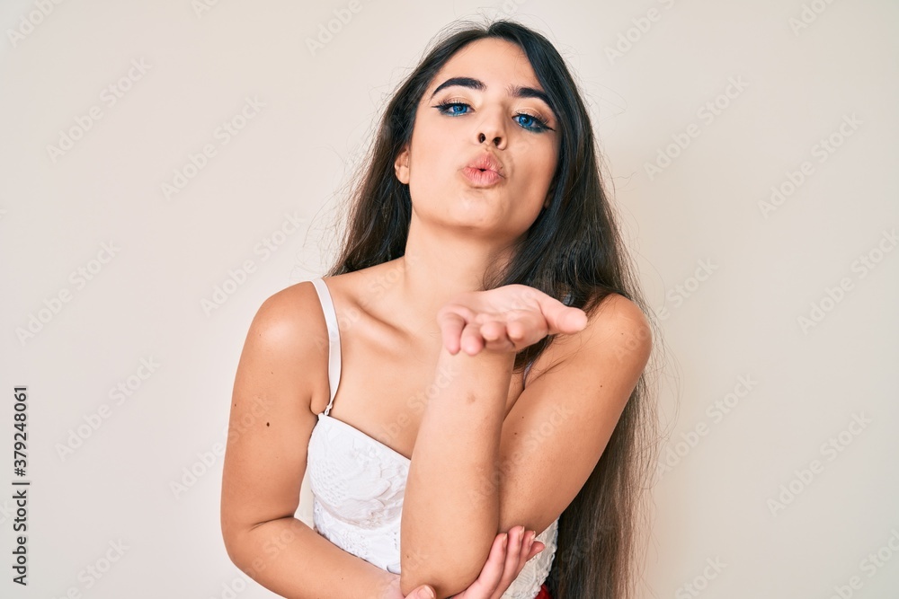 Brunette teenager girl posing elegant looking at the camera blowing a kiss with hand on air being lovely and sexy. love expression. Brunette teenager girl posing elegant looking at the camera blowing a kiss with hand on air being lovely and sexy. love expression.