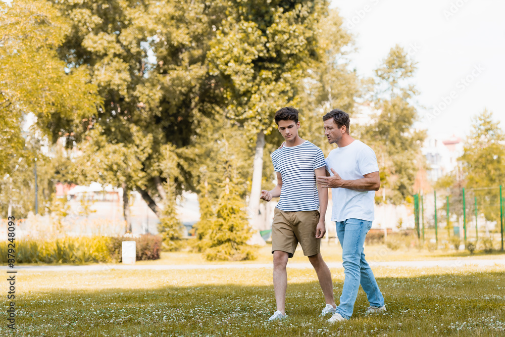 Obraz premium man gesturing while walking and talking with teenager son in park