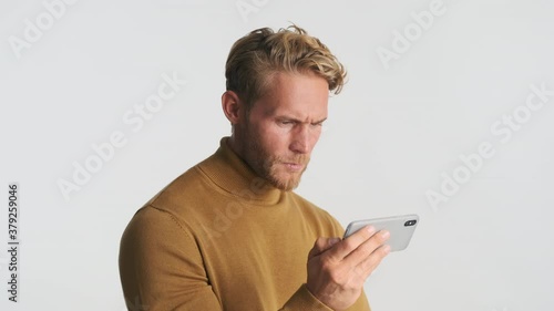 Handsome serious blond bearded man frustratedly watching video on smartphone isolated photo