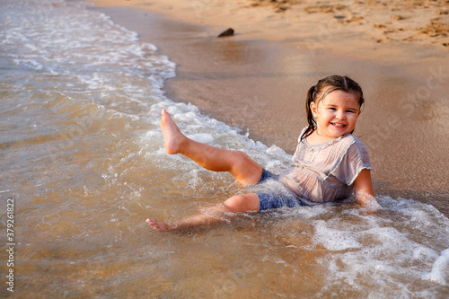 child girl having fun on the sandy beach. sits in the water with waves and laughs