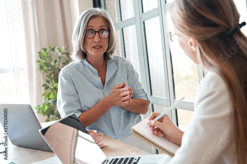 Mature old female mentor or manager training young intern explaining sharing professional skills in office. Middle aged senior business woman teacher speaking to student teaching trainee at meeting.