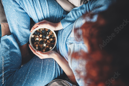 Upper view photo of a curly haired woman in blue pajama eating cereals early morning
