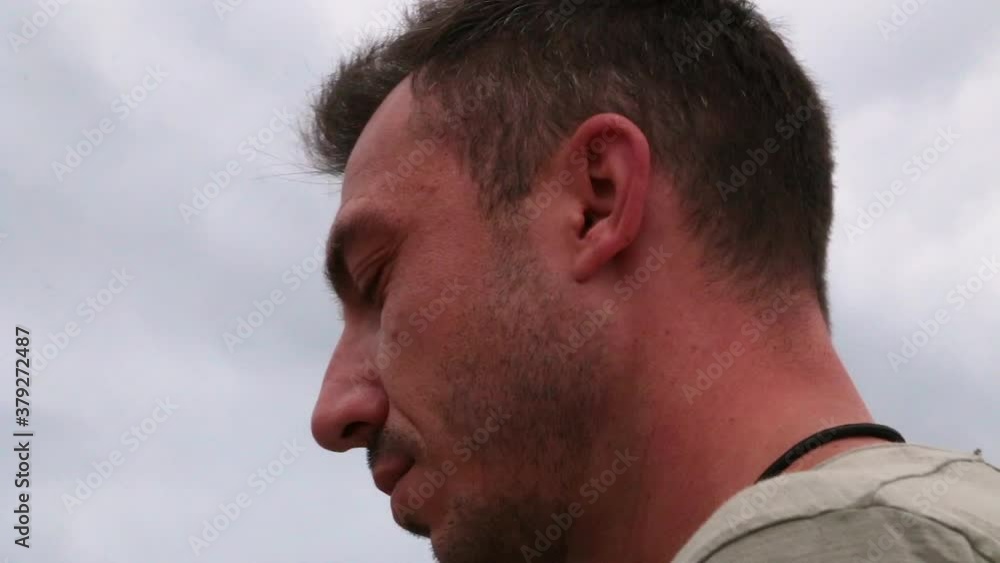 Movement around a young man close-up. The man purposefully looks ahead and shakes his head. Against the background of a gray cloudy sky. Warm soft light. Movement around a young man close-up. The man purposefully looks ahead and shakes his head. Against the background of a gray cloudy sky. Warm soft light.