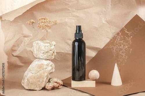 Brown bottle of cosmetic products on stone, wooden geometric shapes on beige paper background. Natural Organic Spa Cosmetic Beauty concept Front view.