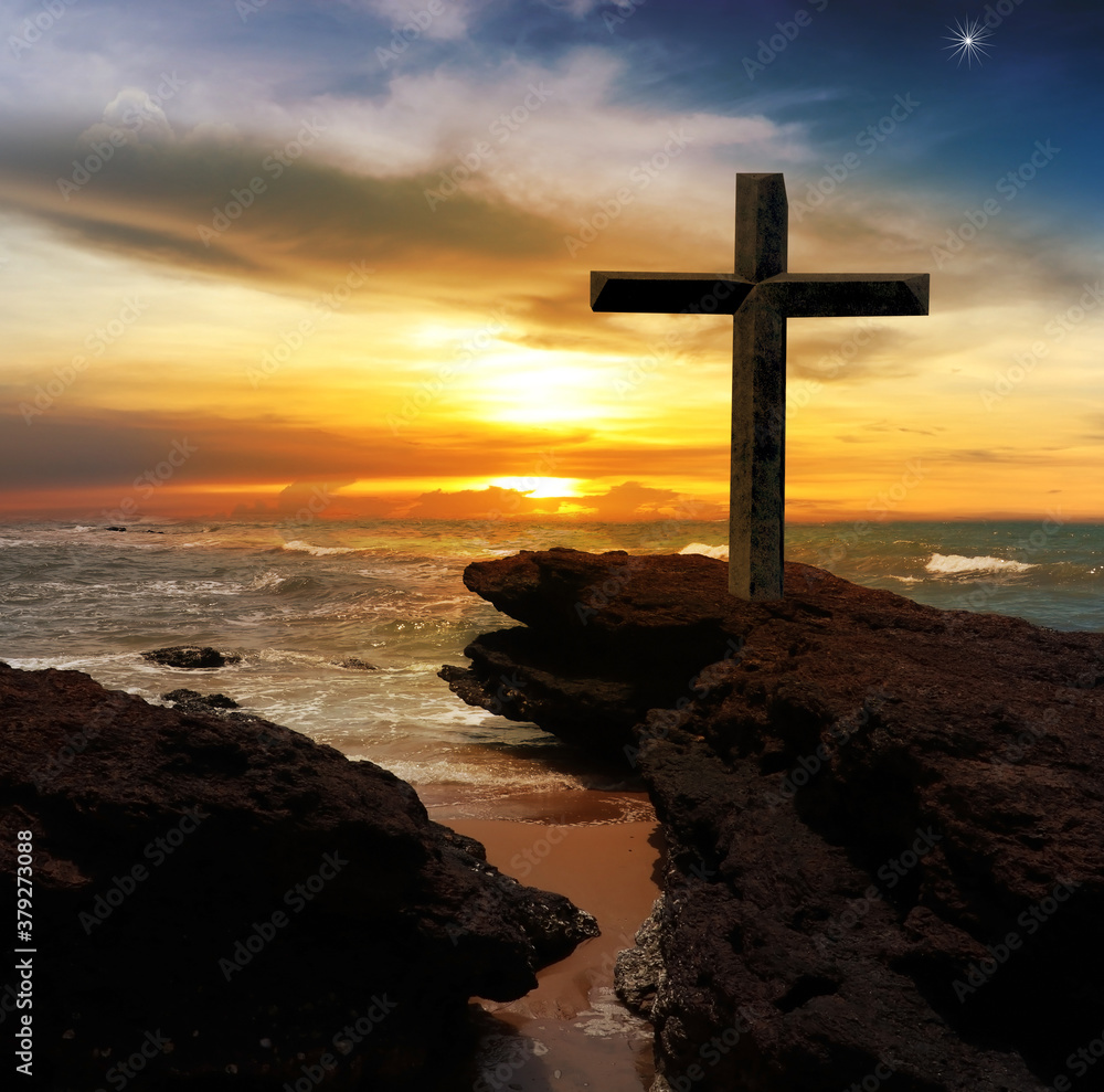 The Cross of Jesus Christ on the rocks by the sea With abstract concept sunset background