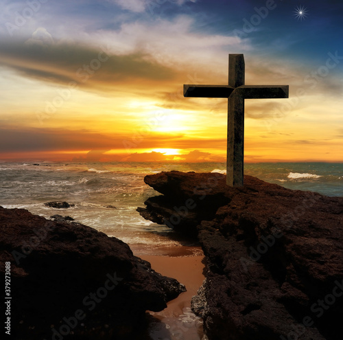 The Cross of Jesus Christ on the rocks by the sea With abstract concept sunset background
