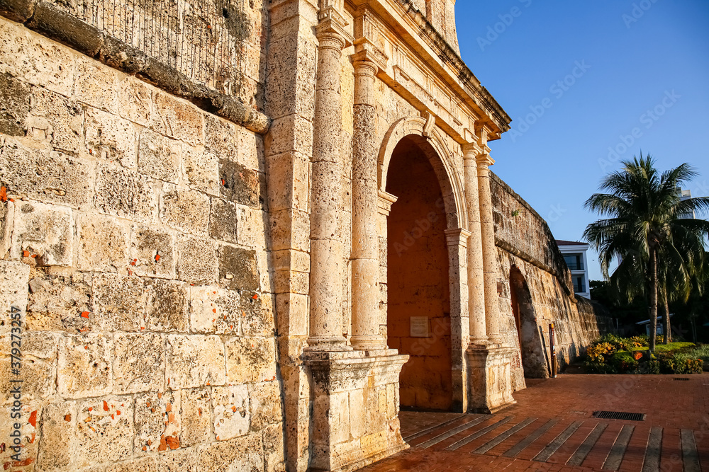 View to an ancient wall and entrance gate in sunshine, palm tree in background, Cartagena, Colombia, Unesco World Heritage