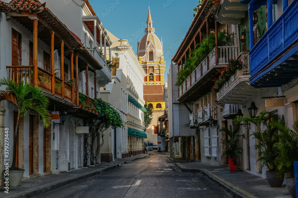 View to the clock tower of Cartagena cathedral with blue sky through a narrow street in shadow, Cartagena, Colombia, Unesco World Heritage
