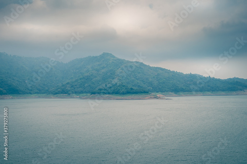 Scenic mountain range next to deep river shrouded in mist landscape view at Thailand.