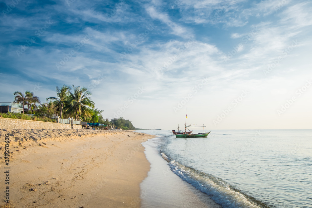 Obraz premium Beautiful view of the turquoise waves with the blue sky and white clouds and fisherman's boat on sandy beach on vacation in Hua Hin, Prachuap Khiri Khan Province, Thailand.