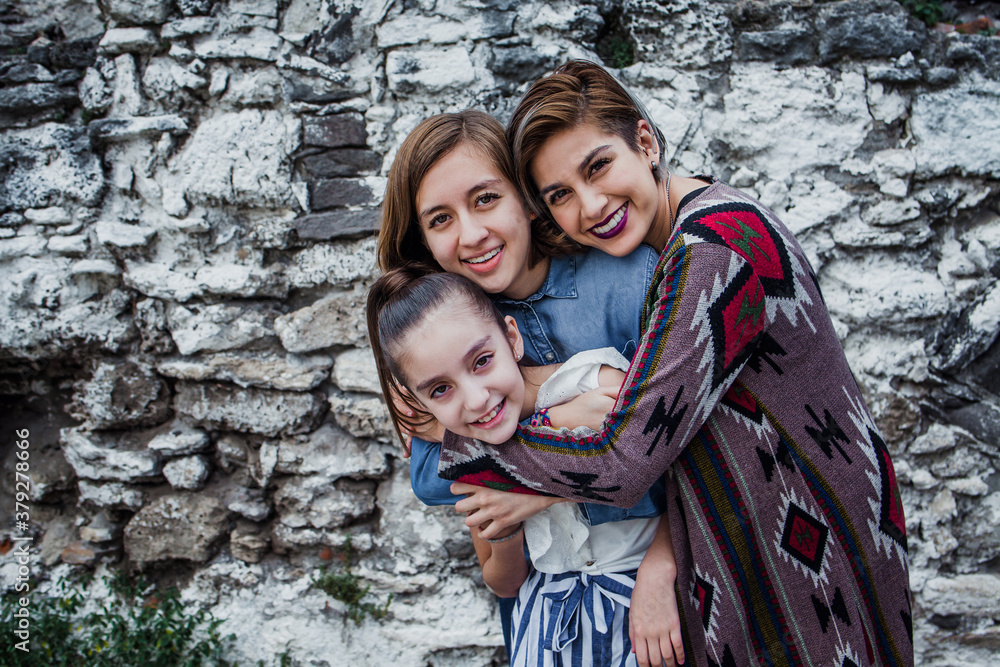 Portrait of three cheerful Mexican sisters hugging and looking at camera in Latin America