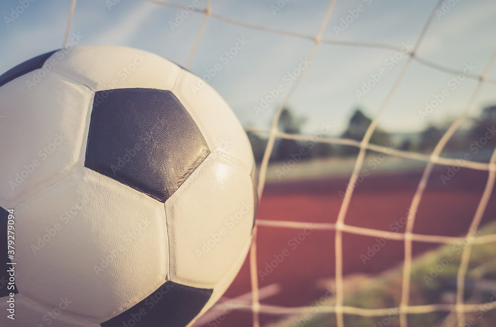 Naklejka premium View of classic leather soccer ball in goal net on blue sky nature background. Traditional black and white football equipment to play competitive game sport tournament concept.