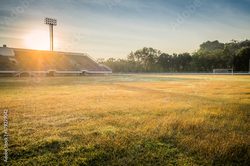 Beautiful sunset over the sport field in stadium. Football arena with green grass and rays of sunlight. Soccer tournament background concept.
