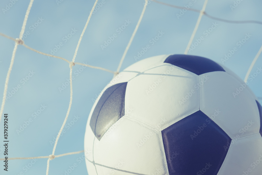 Naklejka premium View of classic leather soccer ball in goal net on blue sky nature background. Traditional black and white football equipment to play competitive game sport tournament concept.