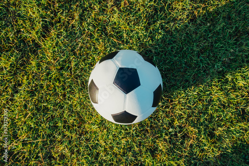 Above view of classic leather soccer ball on green grass field in the arena stadium. Traditional black and white football equipment to play competitive game. Sports tournament. Top view