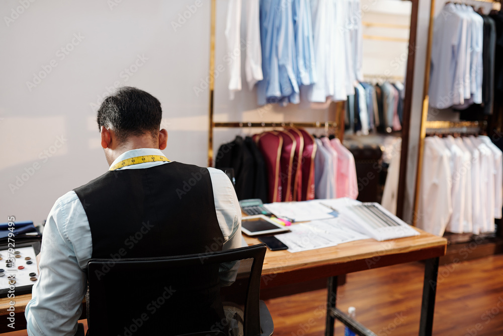 Tailor working at table in atelier, view from the back Tailor working at table in atelier, view from the back