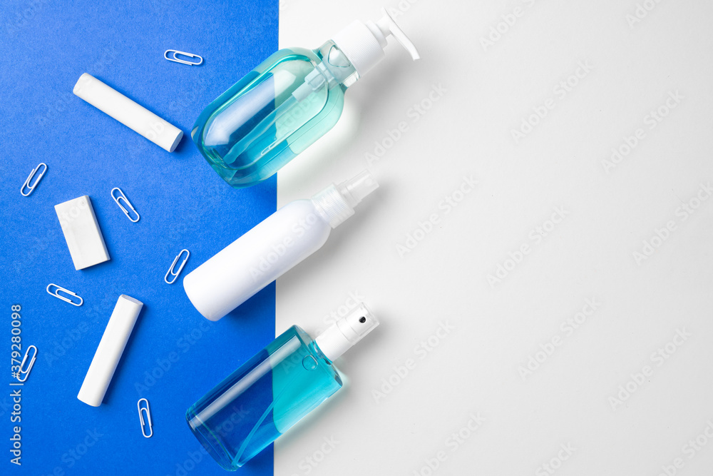 Hand sanitizer and school supplies such as chalks, paper clips on blue and white paper background Hand sanitizer and school supplies such as chalks, paper clips on blue and white paper background