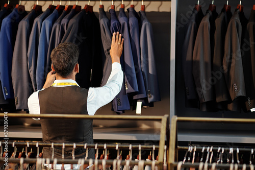 Tailor checking finished bespoke jackets hanging on rail in his atelier