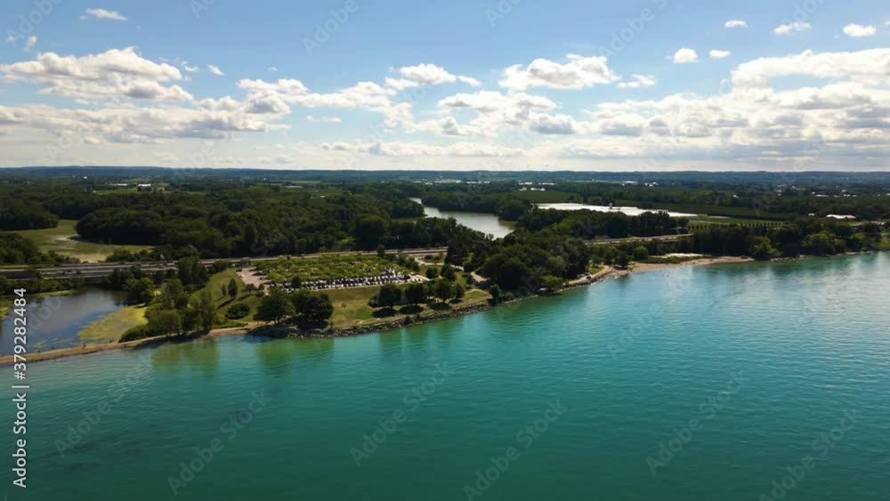Aerial view of the cars driving on a highway along beautiful green blue lake. Cars driving through a natural park next to an emerald lake in Canada. Aerial view of the cars driving on a highway along beautiful green blue lake. Cars driving through a natural park next to an emerald lake in Canada.