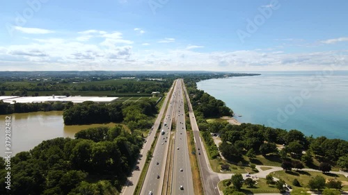 Aerial view of cars driving on a highway next to a beautiful emerald lake. Top view of a cars driving on a highway through green natural park between Lake Ontario and Sixteen Mile Pond in Canada. photo