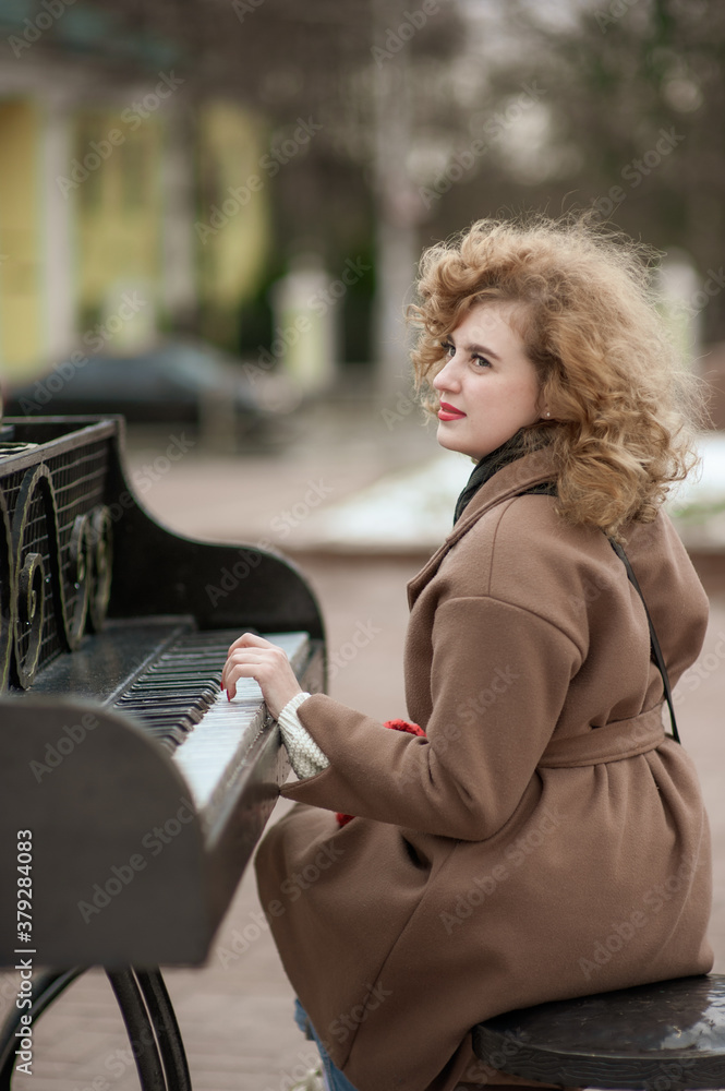 Portrait of a curly-haired girl in a coat, who sits on the street at an old piano. Time for Christmas stories