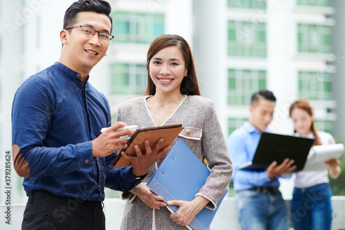 Smiling young Asian business people discussing document on tablet computer and smiling at camera