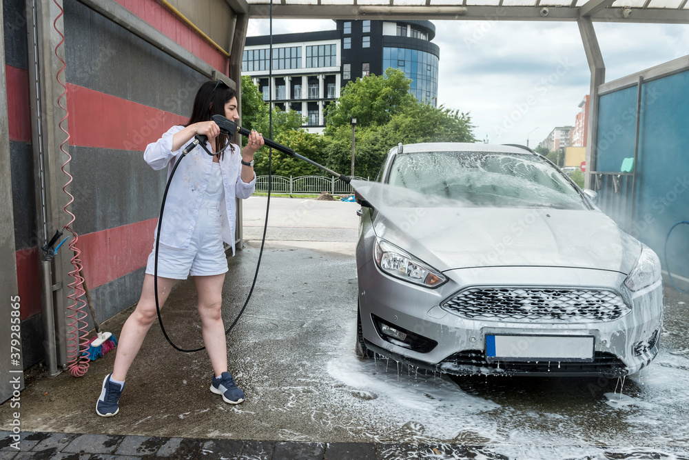 Ukrainian slim woman cleaning and washing foam her car with water jet.
