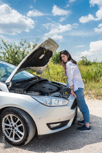 Young woman looks under the engine hood as broken cars motor. Car breakage in road © RomanR